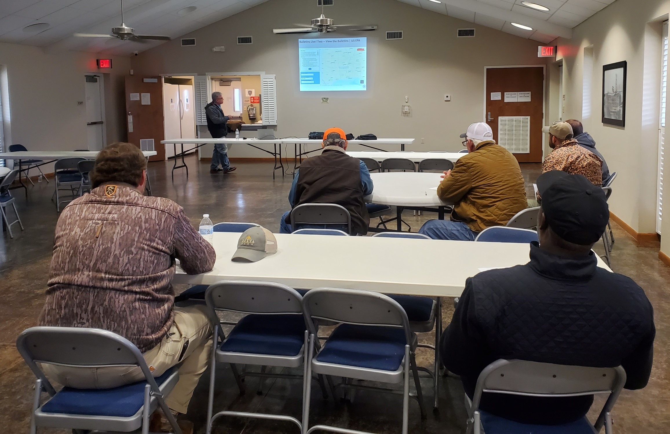 Several men watching a presentation by a speaker.